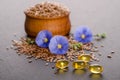 Flax seeds in the wooden bowl, beauty flowers and oil in caps on a grey background Royalty Free Stock Photo