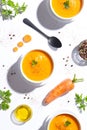 Flay lay, three carrot soup bowls and one carrot on white background. Top view. Vertical format