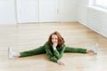 Flexibility, fitness and stretching concept. Attractive redhead female does leg split, stretches legs, wears green sweatsuit,