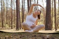 Flexible adorable pregnant woman doing yoga in nature outdoors warming up before training sitting on mat with crossed legs Royalty Free Stock Photo