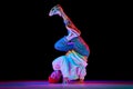 Flexible, artistic young man, breakdancer in motion, performing isolated over black studio background in neon light