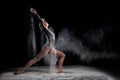 Flexible ballet dancer woman dancing and sprinkle flour on black background