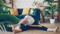 Flexible blonde is doing stretching exercises at home sitting on floor in modern apartment. Girl is bending head to knee Royalty Free Stock Photo