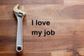 A flexible chromed adjustable wrench lies on a dark wooden table. The solgan I love my job is written on the table in black letter Royalty Free Stock Photo