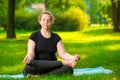 flexible and concentrated woman oversize is meditating on the lawn in the park