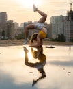Flexible female gymnast doing handstand and calisthenic with reflection in the water on cityscape background during Royalty Free Stock Photo
