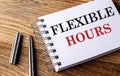 FLEXIBLE HOURS text on notebook with pen on wooden background