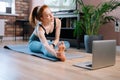 Flexible redhead young woman working out, doing stretching exercise on yoga mat via laptop online Royalty Free Stock Photo