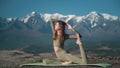 Flexible sportive young woman practices yoga on background of snow-capped mountains