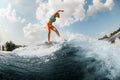 Flexible young woman in colorful swimsuit having fun and balancing on wave on wakesurf board.