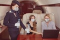 Flight attendant in facial mask as protection from covid-19 serves passengers inside business jet.