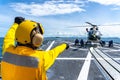 Flight deck officer directs seamen chalk and chain an Eurocopter EC 645 T2 helicopter on the flight deck aboard the guided-