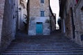A flight of steps in an italian medieval village in front of a ruined abandoned house with a green door Corinaldo, Marche