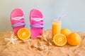 Flip flops, orange juice, oranges, starfishes and seashells on sand beach on blue backdrop. Royalty Free Stock Photo