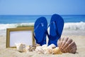 Flip-flops with photoframe and seashells on beach Royalty Free Stock Photo