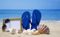 Flip-flops with photoframe and seashells on sandy beach