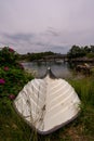 Flipped white boat on the grass by water and Lysefjord Bridge on the horizon,