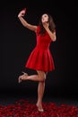 A flirtatious girl in a red dress sends an air kiss and makes selfie. Indoors.