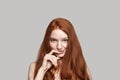 Flirting mood. Portrait of cute young redhead woman smiling at the camera and touching her lips while standing against
