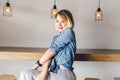 Flirty smiling blond girl with blue eyes and bright pink lips sitting in a coffee shop on a chair drinking coffee. She Royalty Free Stock Photo