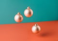 Floating golden Christmas tree baubles against two tone pastel background.