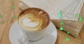 Floating green network icons connecting over white cup with latte art on table beside open book Royalty Free Stock Photo