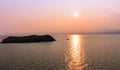 A floating lonely boat passing by the island at sunset Sunset, boat, island, lake, water, sea, pink, orange, evening, summer, res Royalty Free Stock Photo