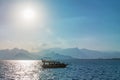 Floating small boat in the sea against the backdrop of relief mountains and a bright sun illuminating the sea surface