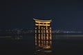 The floating Torii Gate of Itsukushima Shrine Illuminated in the night in front of city lights in Miyajima, Hiroshima, Japan Royalty Free Stock Photo