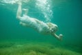 A floating woman. Underwater portrait. Girl in white dress swimming in the lake. Green marine plants, water