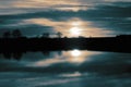 Flood in farmland field meadow at sunset with trees and sun reflected in the water. Climate change concept.