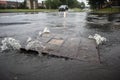 Flood water from rain spouting up through manhole cover on a street road