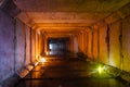 Flooded rectangular sewer tunnel with dirty urban sewage illuminated by color lights and candles