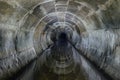 Flooded round underground drainage sewer tunnel reflecting in dirty sewage water