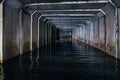 Flooded sewer tunnel is reflecting in water. Dirty urban sewage flowing throw rectangular sewer tunnel