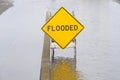 Flooded sign in middle of water flooding street and adjacent parking area