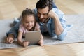 On floor lying daughter with father watching cartoons using tablet