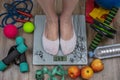 Floor scales with female feet standing, apples, water bottle, measuring tape, dumbbells, fitness rubber bands, a ball Royalty Free Stock Photo