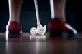 Floorball player standing with stick and ball on. Floor hockey. Back view between sneakers. Dramatic light.