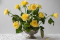 Floral arrangement of yellow garden rose flowers on pin frog in vintage vase. Spring ikebana decor on a lace tablecloth.