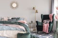 Floral pillow and pink blanket on emerald green comfortable armchair in fashionable bedroom