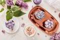 Floral purple cupcakes on the golden tray using trend Dreamy Escapism. Desserts, coffee cup and lilac flowers background