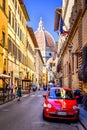 Red small car is parked in narrow street of Florence with view of Basilica Santa Maria del Fiore