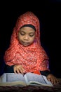 FLORES, INDONESIA-JUNE 25 2014: A girl around 7 years old wearing a hijab is reading the quran on a table with ethnic motifs to