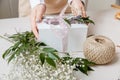 A florist decorates a gift box with flowers and a ribbon on a white desktop. Only the hands are in the frame