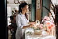 Florist dressed in a striped dress collections a bouquet in the basket from fresh flowers of pastel colors in the flower