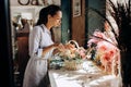 Florist dressed in a striped dress collections a bouquet in the basket from fresh flowers of pastel colors in the flower