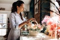 Florist dressed in a striped dress collections a bouquet in the basket from fresh flowers of pastel colors in the flower