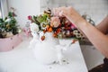 A florist makes a bouquet of different flowers and rose hips in a white vase at a white table in his workshop Royalty Free Stock Photo