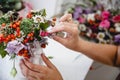 A florist makes a bouquet of different flowers and rose hips in a white vase at a white table in his workshop Royalty Free Stock Photo